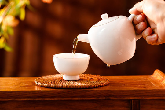 人拿著白色茶壺向茶杯倒茶