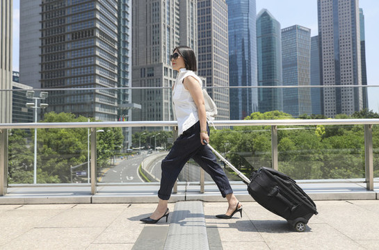 商務(wù)女士手拉旅行箱走在街道