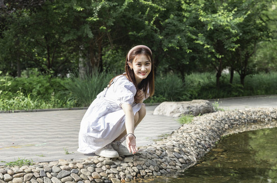 蹲在水潭邊玩水的美麗東方女孩