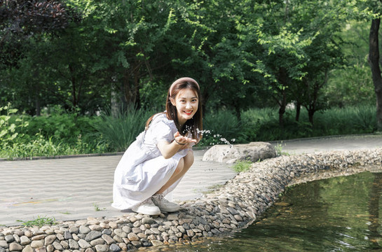 蹲在水潭邊玩水的美麗東方女孩