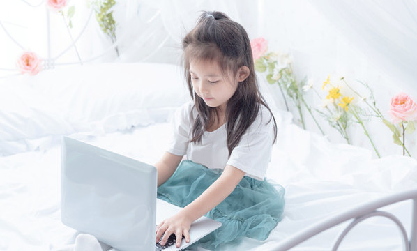 床上手持電腦的小女孩