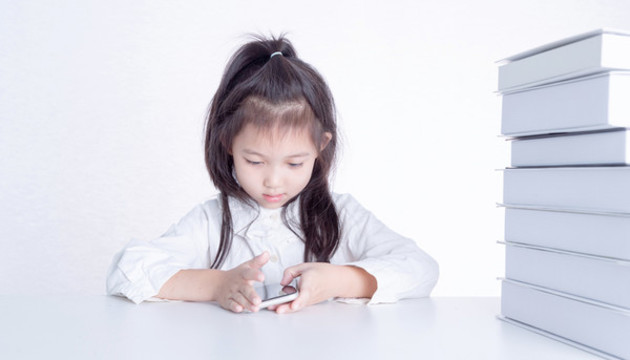 書桌上使用手機的小女孩