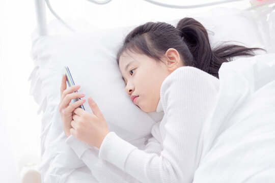 床上使用手機的小女孩