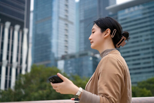辦公樓外行走的職業(yè)女性手持手機(jī)