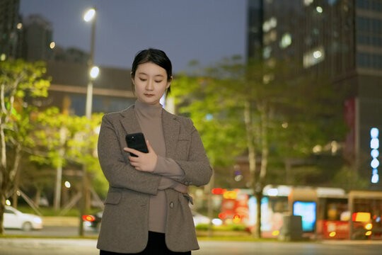 走在夜晚人行道上看手機的女性