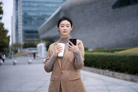城市景觀中職業(yè)女性喝咖啡看手機(jī)