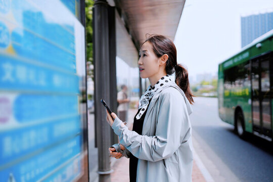 公交車站的女人用手機(jī)查看時(shí)刻表