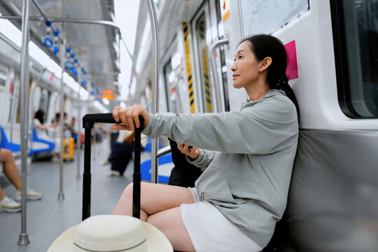 女性拿著行李和手機在地鐵上思考