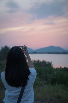 女人拿著手機(jī)拍攝夕陽(yáng)天空風(fēng)景