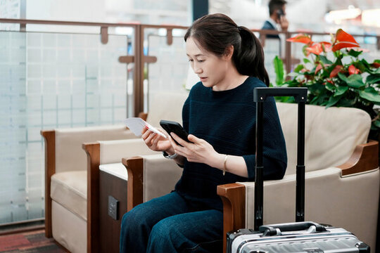 女子拿著智能手機和行李在機場等候