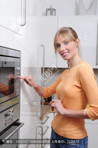 金發(fā)女人在現(xiàn)代廚房里用微波爐做飯