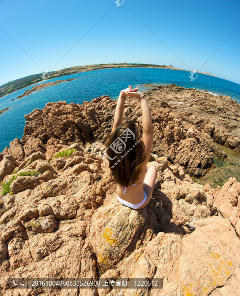 美麗的女人放松在巖石與海景在撒丁島；意大利