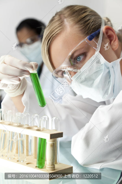 一個金發(fā)碧眼的醫(yī)學或科學研究人員或醫(yī)生用綠色的解決方案在實驗室與她的亞洲女同事的焦點在她身后。