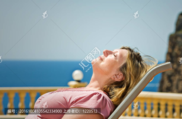 一個年長的女士對沿海的背景拍攝的日光浴