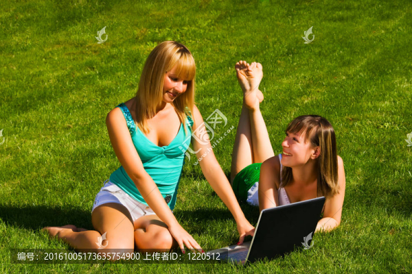 兩個年輕女孩在草地上用筆記本