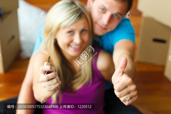 女人和男人拿著鑰匙豎起大拇指。買新房子