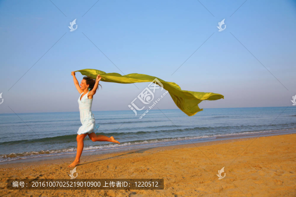 小姑娘手拿黃色織物披肩在海邊奔跑