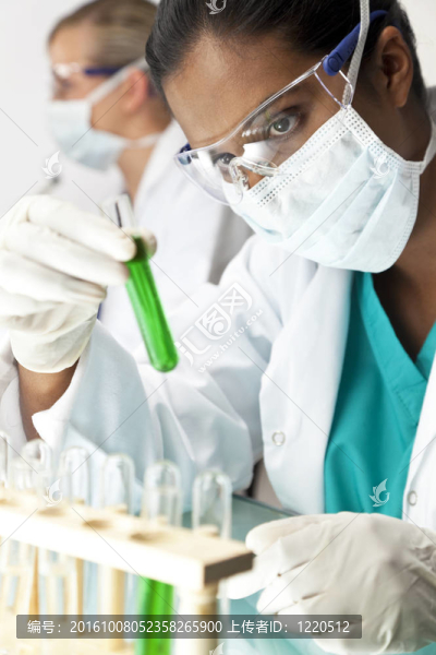 一個亞洲醫(yī)學或科學研究人員或醫(yī)生，在實驗室里看著一個綠色的解決方案，與她的女同事在她身后的焦點。