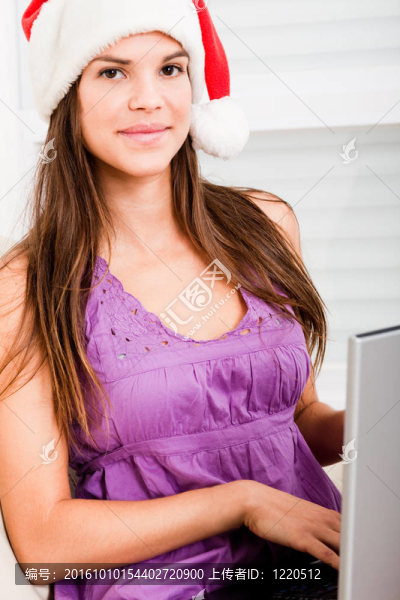 美麗的年輕婦女戴圣誕老人的帽子使用筆記本電腦