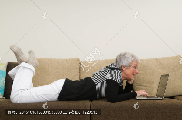 在筆記本電腦上工作的高級婦女；坐在沙發(fā)上放松。