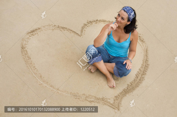 美麗的女孩坐在心在海灘上