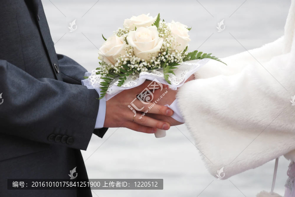 手拉手的新婚夫婦拿著由美麗的白色玫瑰的花束