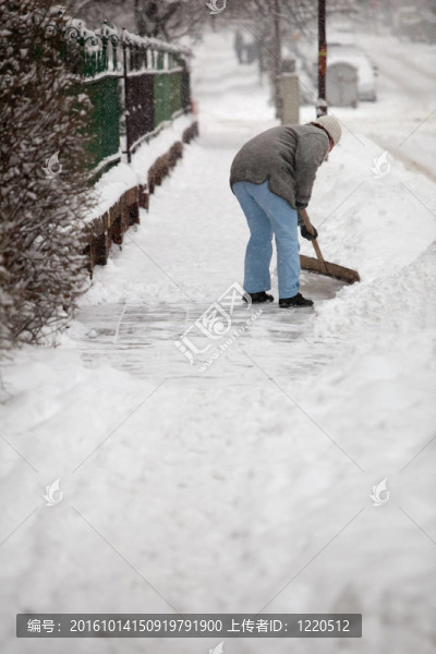 女人鏟人行道上的雪在他的房子前面的一個(gè)城市，大雪之后（在前景上籬笆，重點(diǎn)）