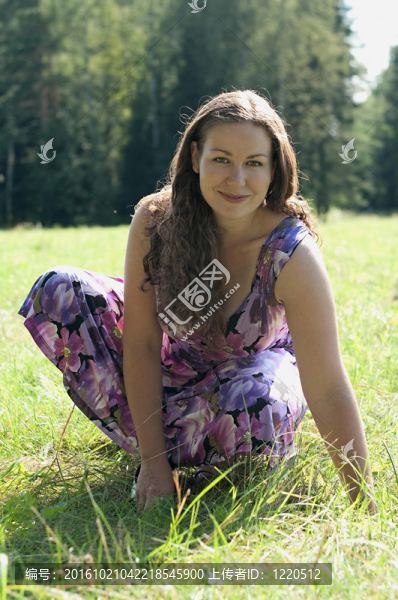 穿著淺色連衣裙的年輕女子坐在草地上微笑。陽光夏令時(shí)。