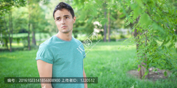 在一個可愛的夏日公園里，一個英俊的年輕人在公園里散步的照片