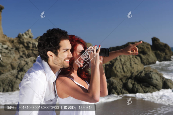 海灘上的年輕夫婦透過雙筒望遠(yuǎn)鏡
