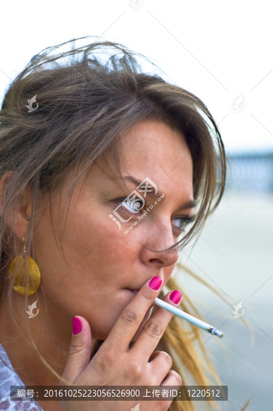 年輕漂亮的女孩抽煙。紫色的指甲。海灘上的夏日肖像。模糊焦點(diǎn)。