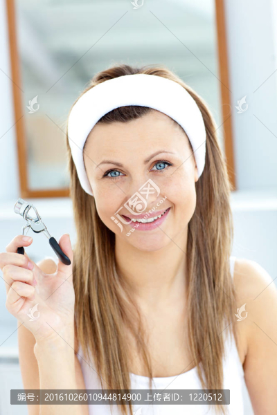 微笑的女人拿著睫毛夾看著相機(jī)在家里的浴室