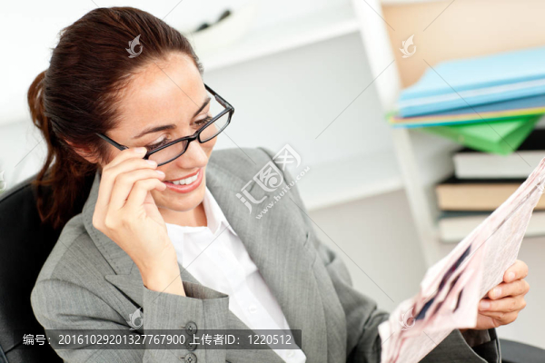 開朗的女商人抱著她的眼鏡看報(bào)紙?jiān)谒霓k公室里，坐在書桌前