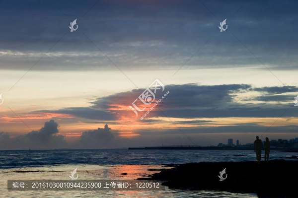 夕陽下牽手漫步海灘的年輕情侶剪影