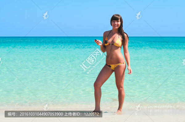 年輕性感的女孩站在海邊的沙灘上聽音樂。側(cè)