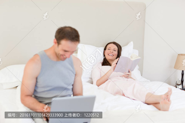 當(dāng)他的妻子正在床上看書的時(shí)候，男人在他的筆記本電腦上工作