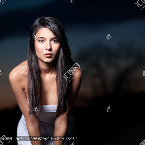 一幅年輕的肖像；美麗的女人；在外面拍攝；在日落的背景。她戴著一頂白色的上衣；她看著相機；她微笑著向前