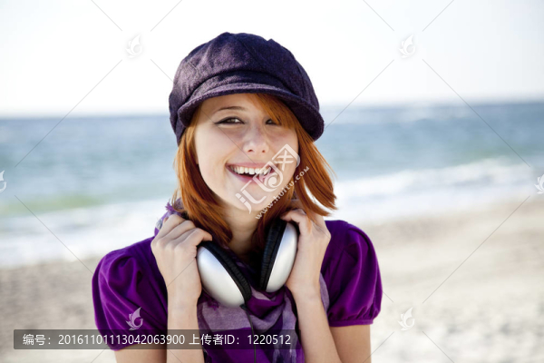 在海灘上帶著耳機的紅頭發(fā)女孩肖像。