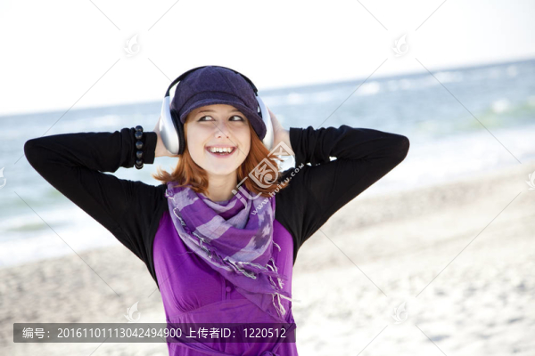 在海灘上帶著耳機(jī)的紅頭發(fā)女孩肖像。