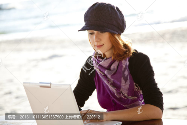在海灘上與筆記本電腦的紅頭發(fā)女孩肖像。