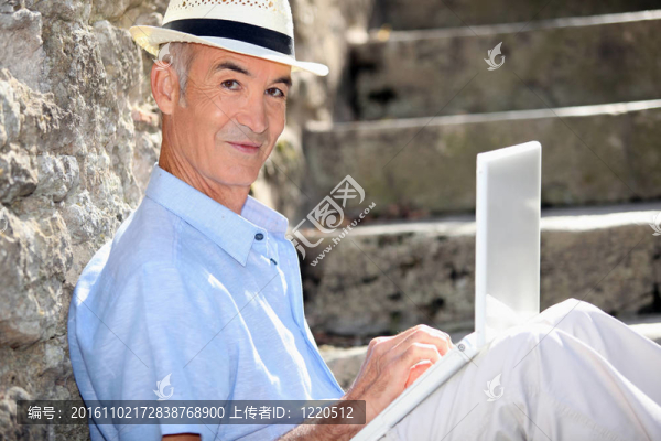 退休男子與筆記本電腦靠墻坐