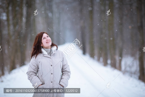 享受著第一場(chǎng)雪：在一個(gè)可愛的森林路徑看雪花飄落的年輕女子（顏色色調(diào)的圖像）