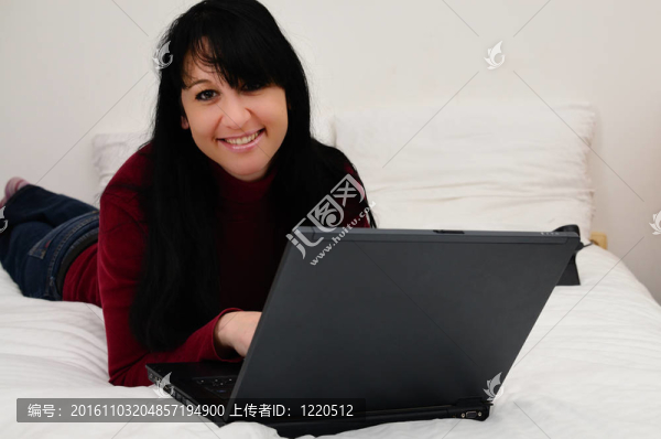 可愛的年輕女子與筆記本電腦在床上