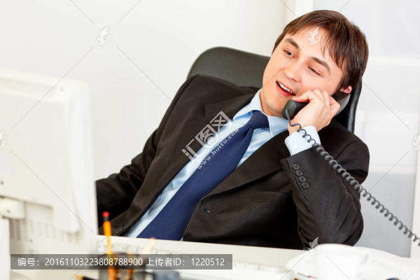 高興的商人坐在辦公桌前，用電話交談