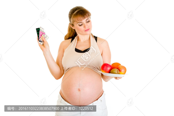 憂郁的孕婦選擇藥片和水果之間的白色隔離