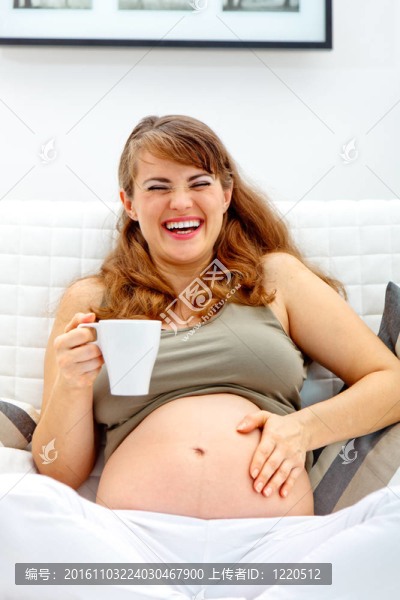 笑著漂亮的孕婦坐在沙發(fā)上，手里拿著一杯茶