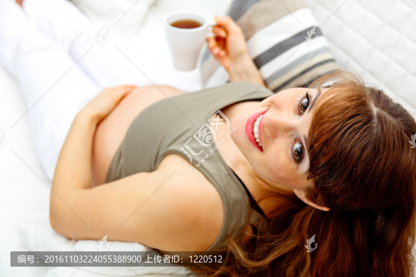 微笑美麗懷孕女性在沙發(fā)上放松與家中的一杯茶。特寫。