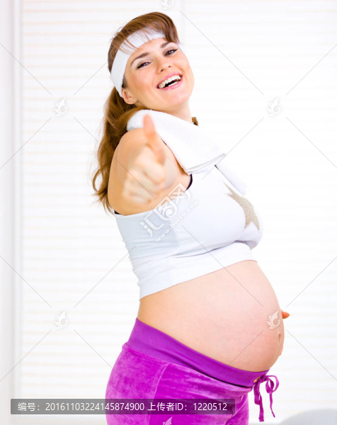 微笑美麗的孕婦抱著她的肚子和豎起大拇指手勢