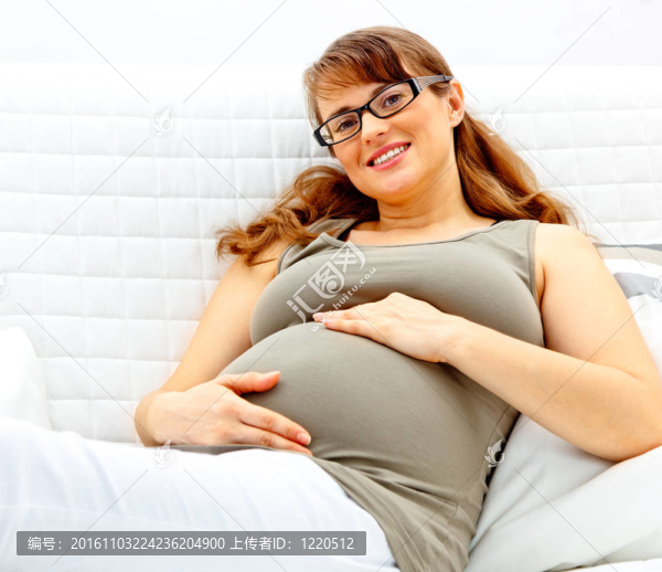 微笑美麗的孕婦躺在家里的沙發(fā)上，抱著她的肚子。