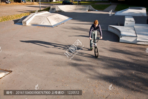 年輕的紅頭發(fā)的男孩是他的自行車在玩滑板公園跳